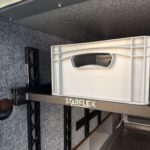 Detaljbilde av Starflex teleskoprør festet i modulskinne på vegg, med euroboks plassert stabilt på hyllearm.